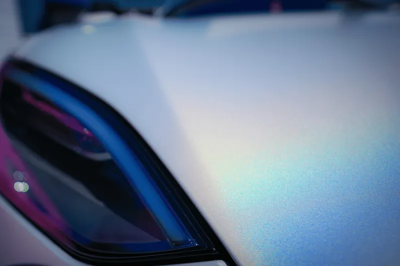 Close-up of an iridescent color-shift film shifting from blue to pink across a body panel